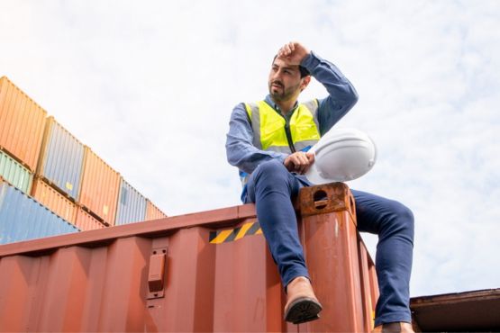 A construction worker overheating on a shipping container