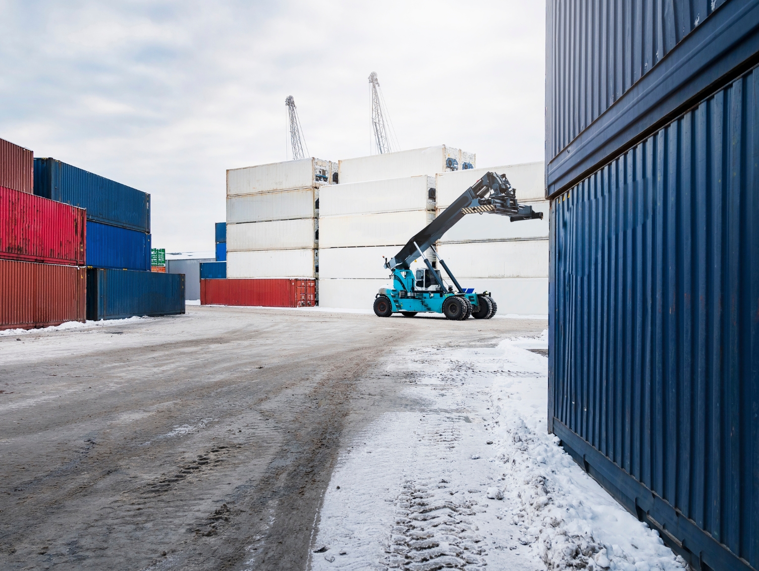 Stacked shipping containers in a snowy yard with a reach stacker vehicle operating between them, illustrating Christmas Philspace Shipping Containers