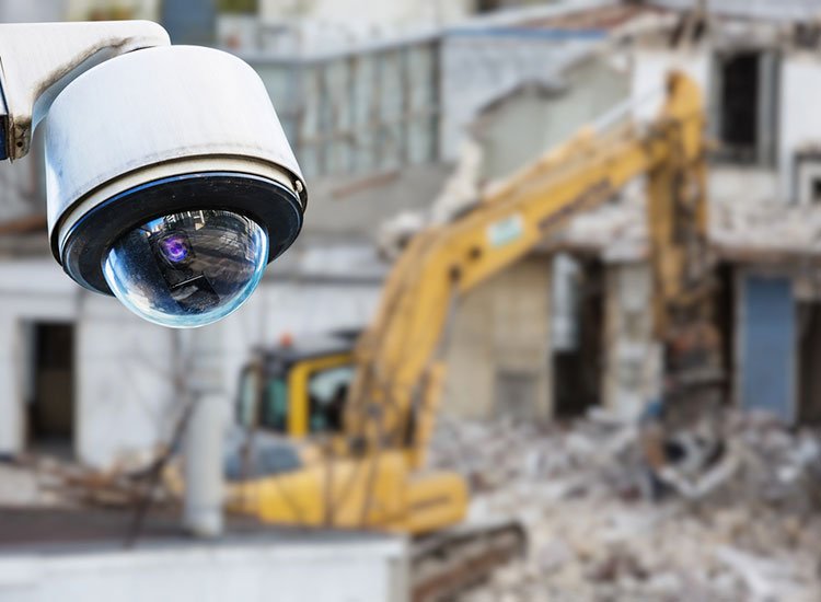 A CCTV camera in the top left corner of the image in the foreground, with a blurred construction equipment in the background
