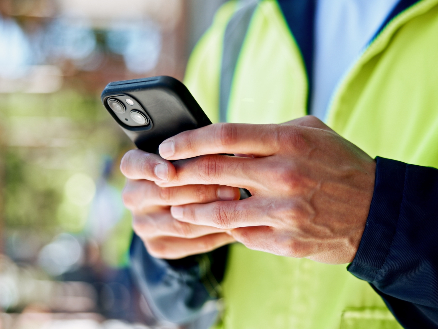 A close-up of a worker in a high-vis jacket using a smartphone outdoors, reflecting operational planning for organising shipping containers for Christmas Philspace