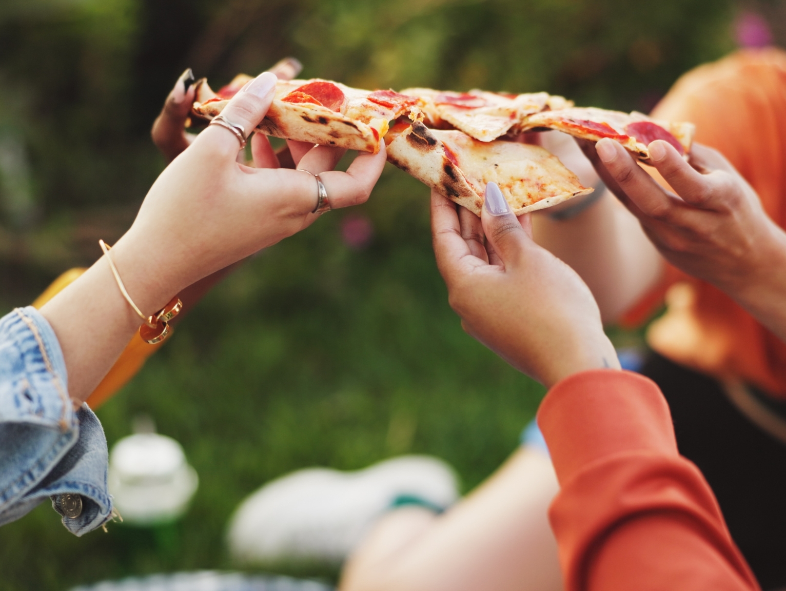 Shipping container restaurants: People outdoors sharing slices of pizza, with hands holding and pulling apart slices in a casual, social setting.