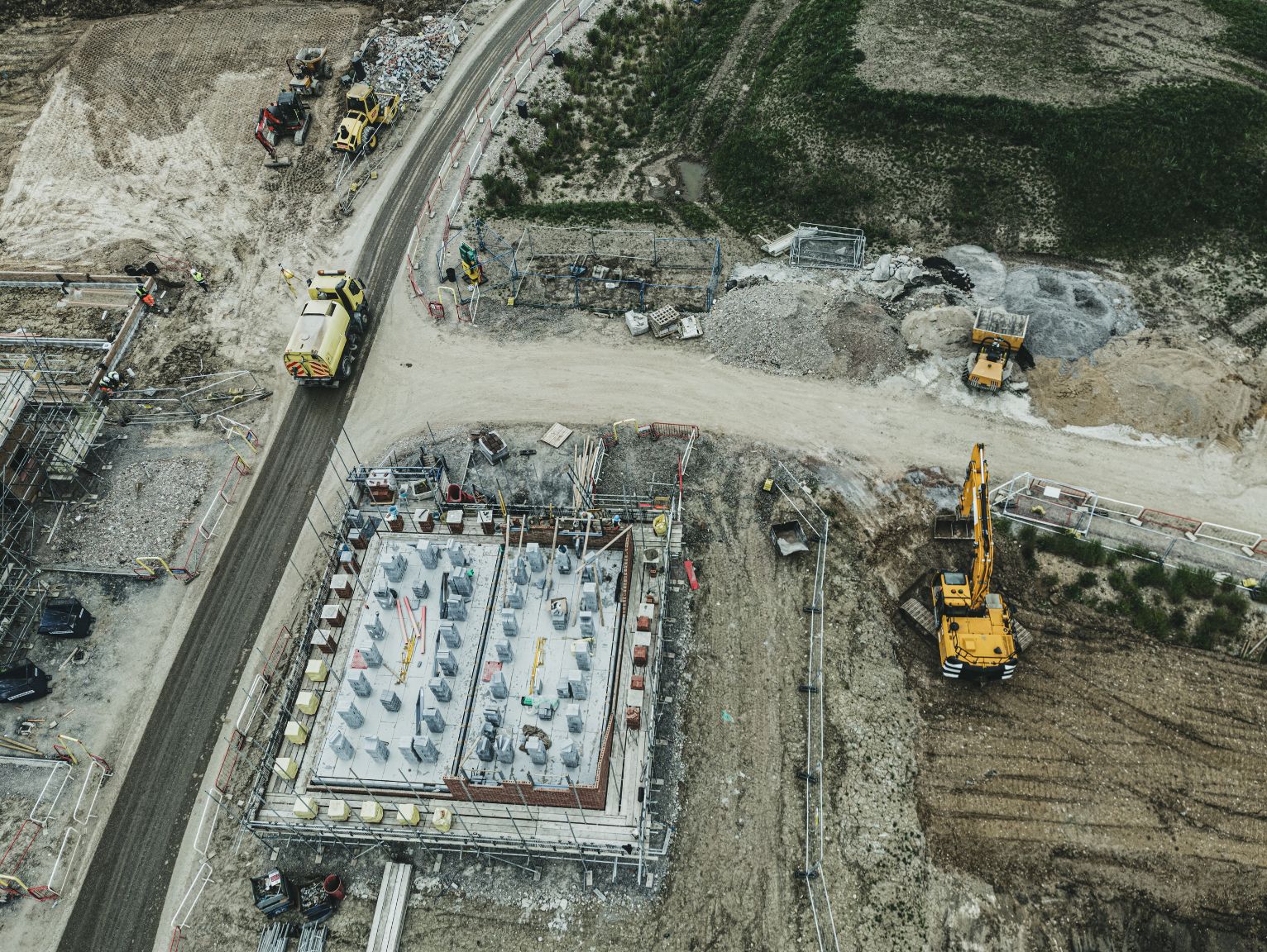 Supporting welfare needs on short-duration site work: An aerial view of a large infrastructure construction site, showing yellow heavy machinery, a concrete foundation, access roads, and workers in high-visibility jackets.