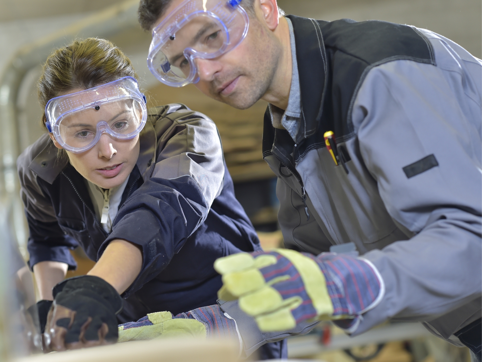 Two construction apprentices wearing safety goggles and gloves focused on hands-on training in a workshop.