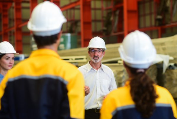 Construction site supervisor leading a safety or training briefing with workers in hard hats and high-vis jackets.