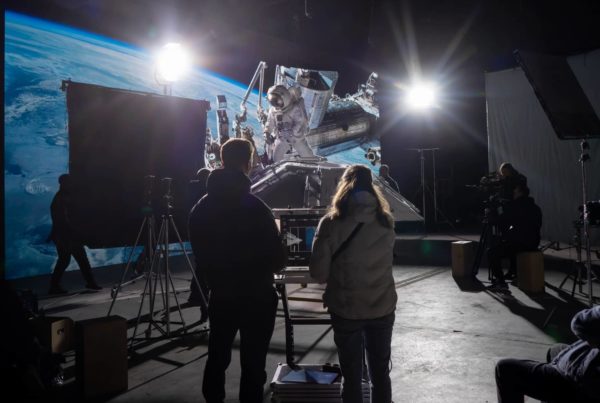 Film crew shooting scene with astronaut visuals on large screen