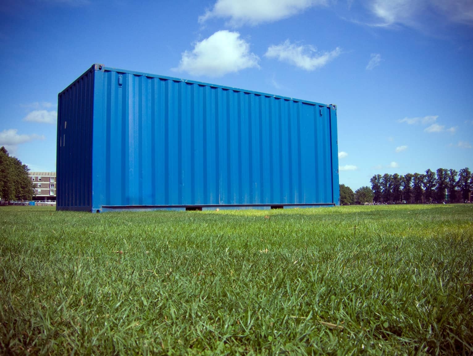 Blue shipping container placed on a grassy lawn under a blue sky